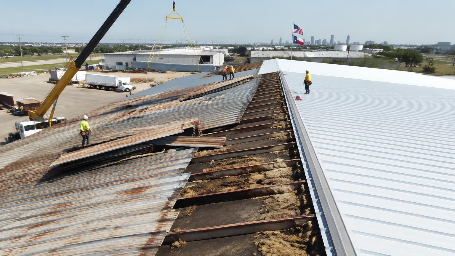 Commercial metal roof replacement in progress on a Texas warehouse, old rusted panels being removed beside new white panels with a crane lifting materials