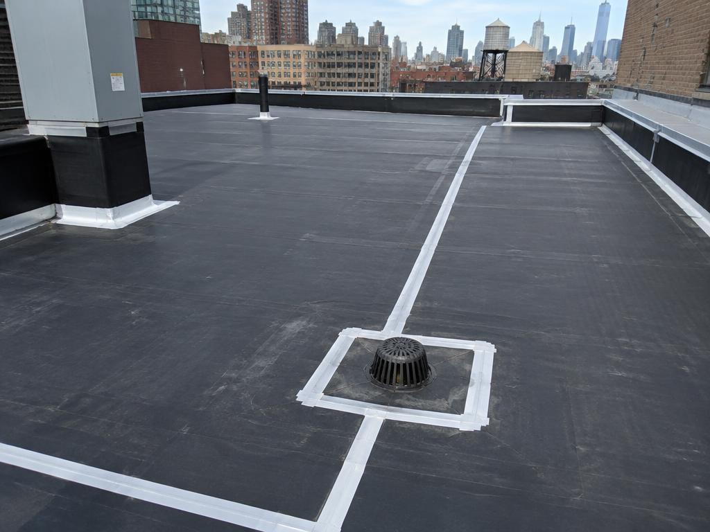 A black EPDM rubber roof with white seam tape and a roof drain on a New York City commercial building